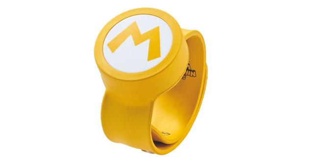 Imagem da Power-Up Band especial, uma pulseira dourada com um grande M do Mario ao longo da pulseira e o logo do parque temático Super Nintendo World.